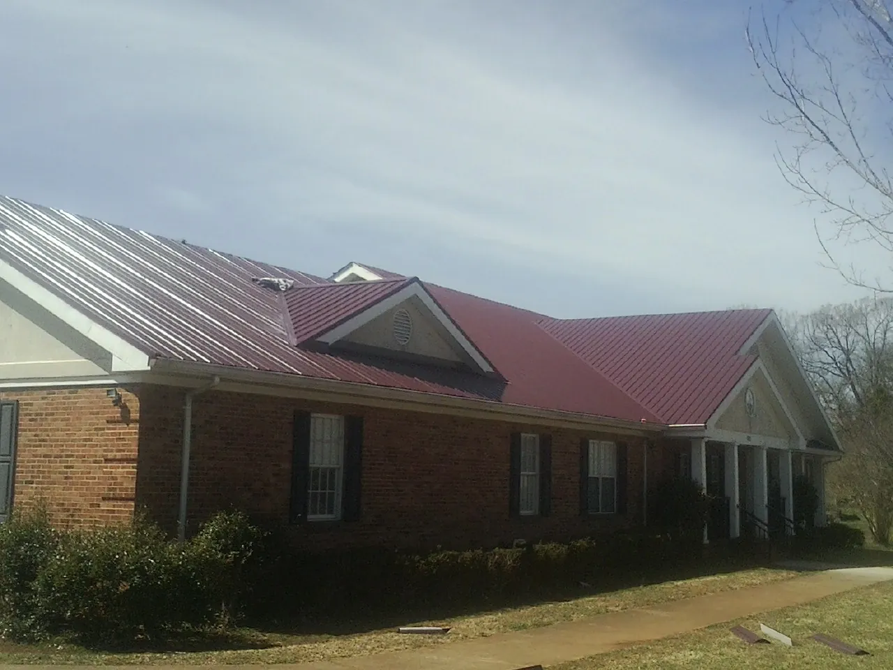 Red metal roof with gabled entries on a long brick building, from a Hail Damage Roof Repair job in Firth