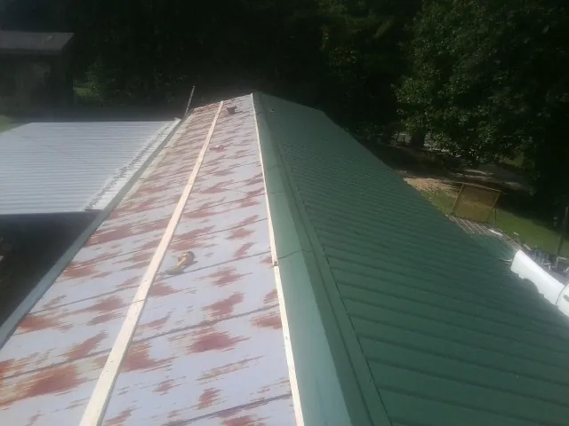Old rusted panels beside newly installed green metal roofing — Wind Damage Roof Repair by Roofing Brothers in Firth