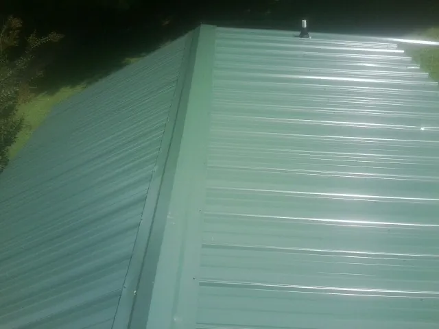 New green metal panels meeting at the ridge of a roof — Flat Roof Repair work by our crew in Firth