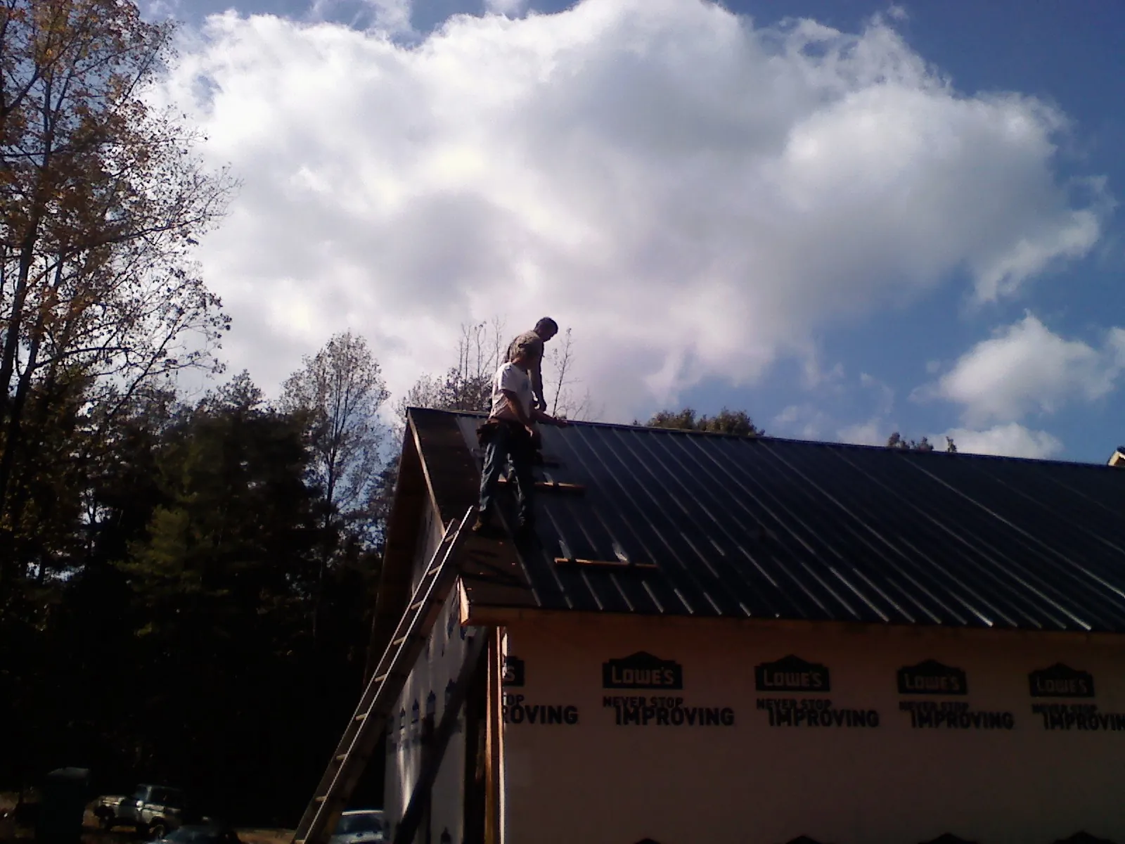 Roofer fastening dark metal panels high against a cloudy sky, from a Roof Inspection job in Firth